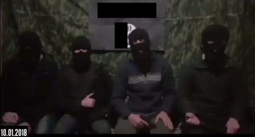 Four masked men sitting at the background of the IS'* flag call on their followers to kill Russian rights defenders. Screenshot of the video. Four masked men sitting at the background of the IS'* flag call on their followers to kill Russian rights defenders. Screenshot of the video.
