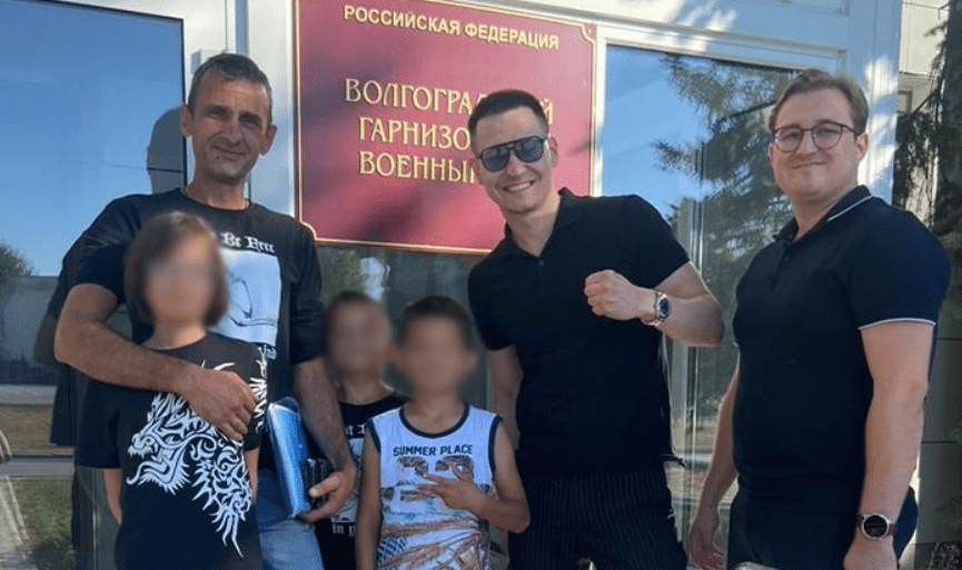 Ruslan Zhadaev (left) with children and protection. Screenshot of the photo "Height 102" from 31.08.25, https://v102.ru/news/147301.html