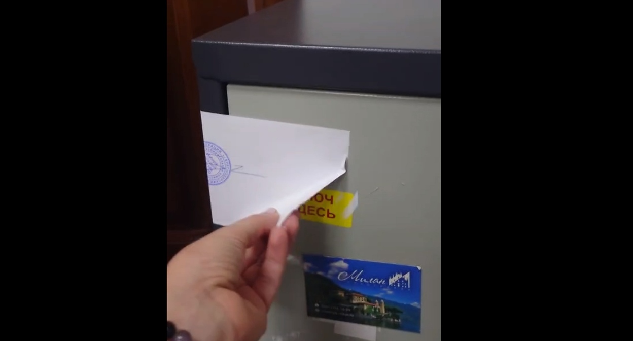 The author of the video demonstrates the peeled corner of the paper that seals the safe. Frame from the video of the Telegram channel "TIK Western Voting 2026" https://t.me/tikzapad/91 The author of the video demonstrates the peeled corner of the paper that seals the safe. Frame from the video of the Telegram channel "TIK Western Voting 2026" https://t.me/tikzapad/91