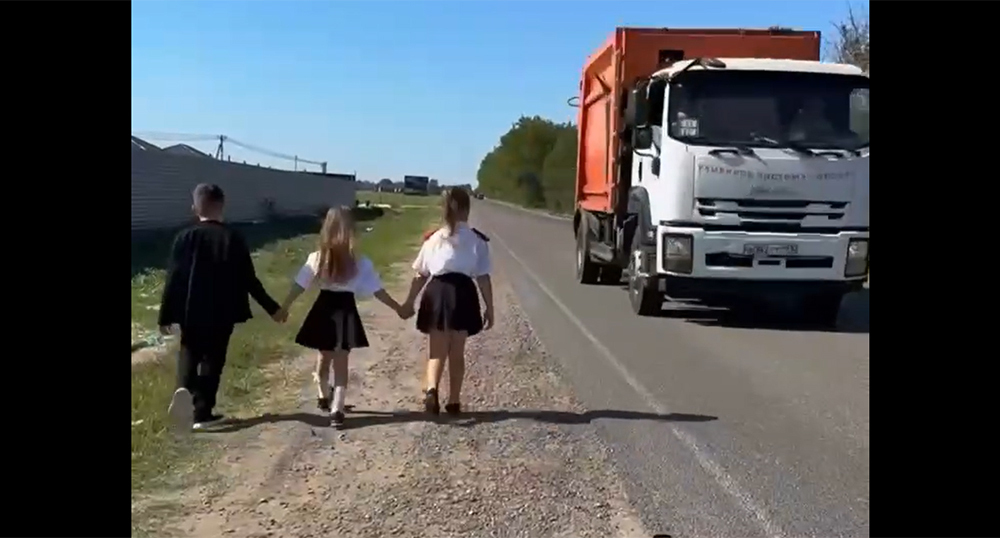 Children walk along the edge of the road due to the lack of a sidewalk. Frame from the video https://t.me/tipichkras/83286 Children walk along the edge of the road due to the lack of a sidewalk. Frame from the video https://t.me/tipichkras/83286